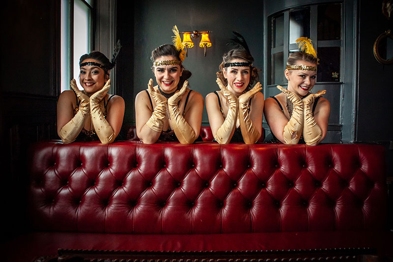 4 gatsby dancers smiling behind a sofa